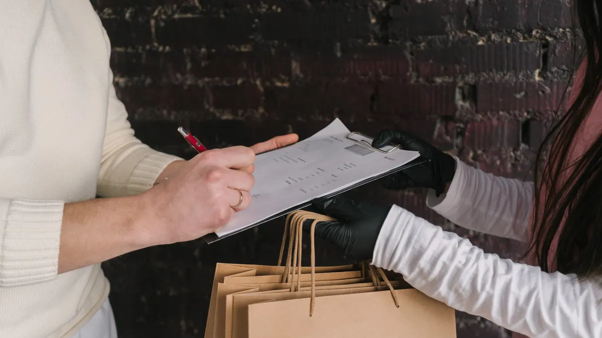 Person checking a clipboard beside shopping bags