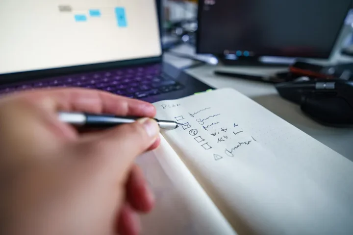 hand writing a checklist beside a computer desk