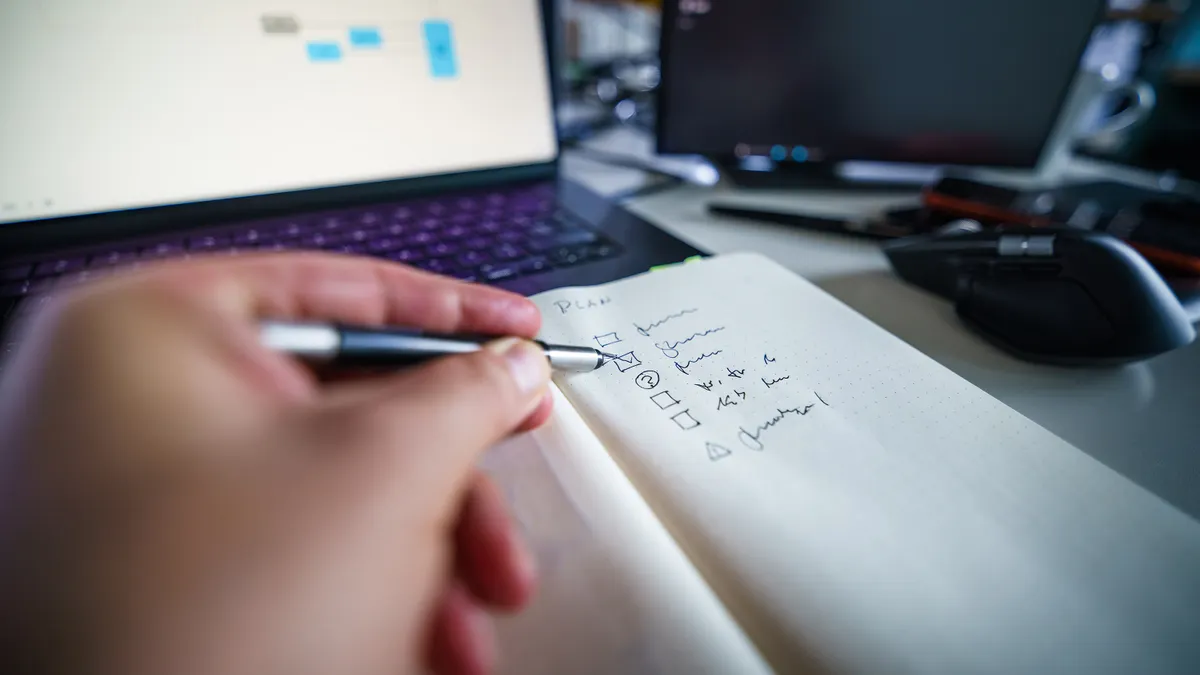 hand writing a checklist beside a computer desk